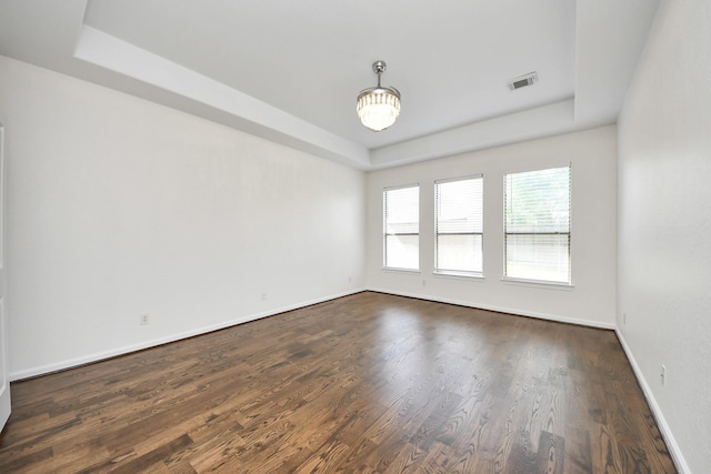 empty room featuring a raised ceiling, dark wood-type flooring, baseboards, and visible vents