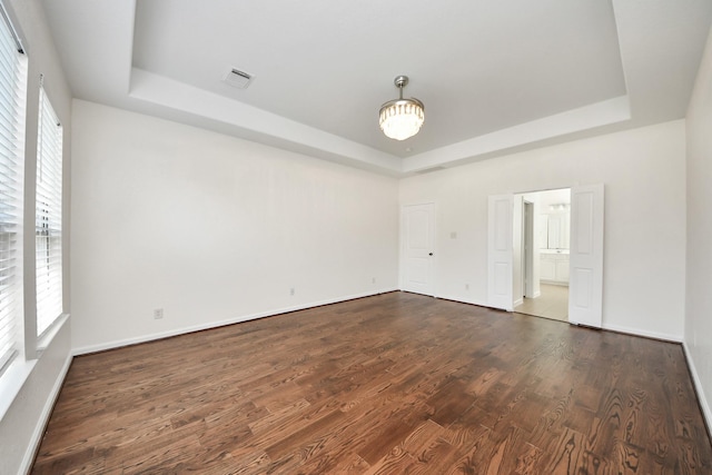 spare room with a tray ceiling, dark wood-type flooring, visible vents, and plenty of natural light