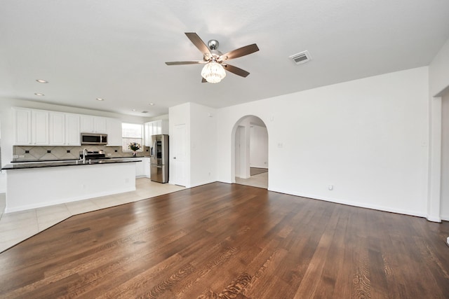 unfurnished living room featuring visible vents, light wood-type flooring, a ceiling fan, and arched walkways