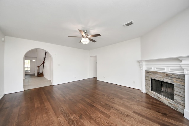 unfurnished living room featuring a fireplace, arched walkways, a ceiling fan, visible vents, and wood finished floors