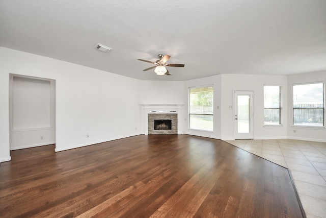 unfurnished living room featuring wood finished floors, ceiling fan, a fireplace, and a wealth of natural light