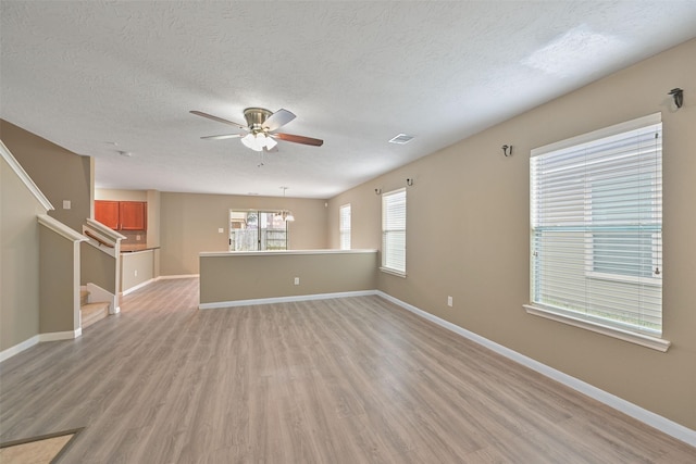 unfurnished living room featuring baseboards, ceiling fan, light wood-type flooring, a textured ceiling, and stairs