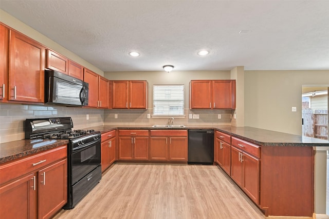 kitchen featuring light wood-style flooring, a peninsula, black appliances, a sink, and decorative backsplash
