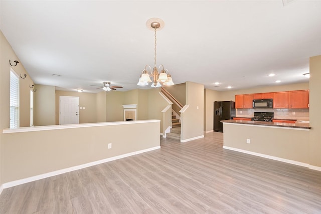 unfurnished living room with stairway, light wood-style floors, baseboards, and ceiling fan with notable chandelier