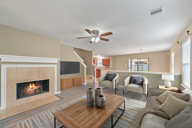 living area featuring a tiled fireplace, visible vents, ceiling fan, and light wood-style floors