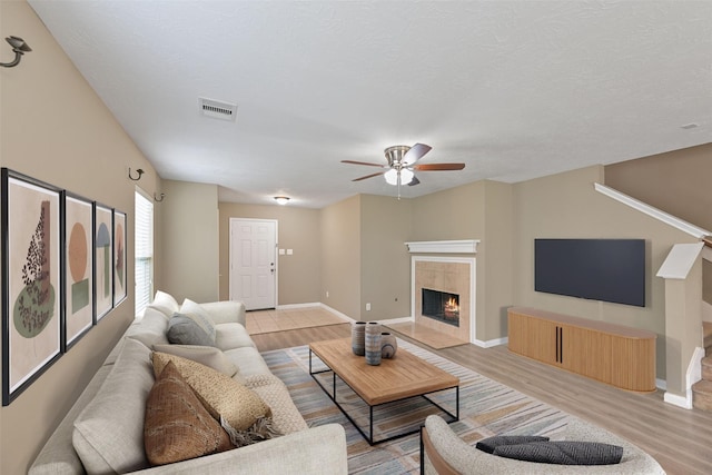 living room featuring light wood-type flooring, baseboards, visible vents, ceiling fan, and a tile fireplace