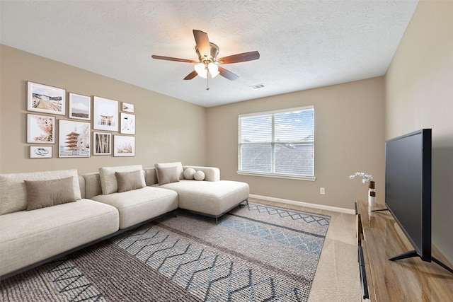 living room with baseboards, a textured ceiling, a ceiling fan, visible vents, and light colored carpet