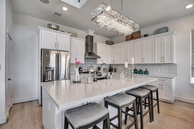 kitchen featuring white cabinets, high end refrigerator, wall chimney range hood, and visible vents