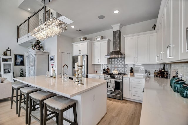 kitchen featuring wall chimney exhaust hood, a kitchen bar, white cabinetry, stainless steel appliances, and light wood finished floors