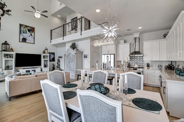 dining area featuring recessed lighting, light wood-type flooring, a towering ceiling, and ceiling fan with notable chandelier