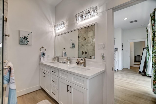 full bathroom with visible vents, a sink, a shower stall, double vanity, and wood finished floors