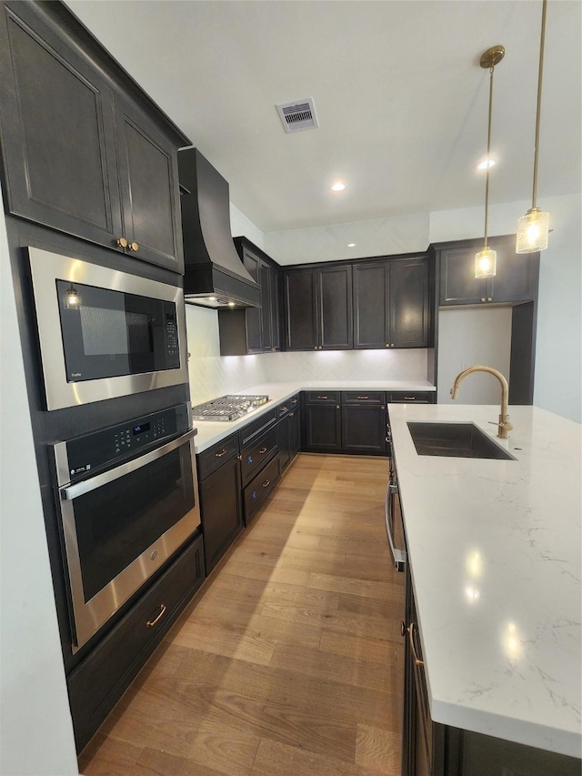 409 Forest Reserve Pl, Houston, TX 77079 - kitchen with appliances with stainless steel finishes, wall chimney range hood, a sink, light stone counters, and hanging light fixtures