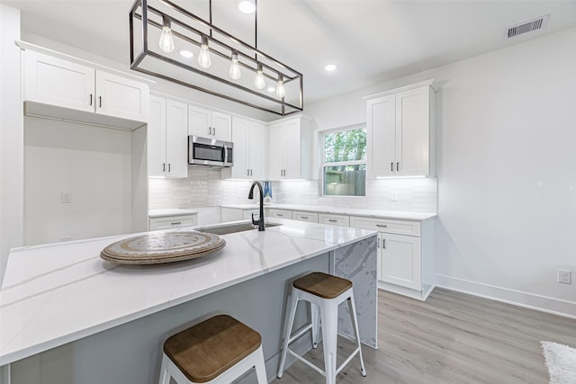 8132 Brandon St, Houston, TX 77051 - kitchen with stainless steel microwave, white cabinetry, backsplash, visible vents, and a sink