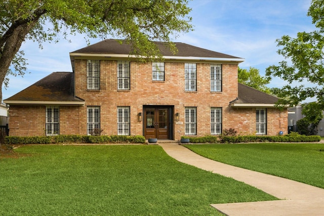 colonial inspired home with a shingled roof, a front yard, and brick siding