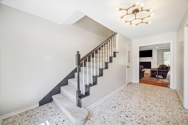 stairs with a chandelier, a fireplace, and baseboards