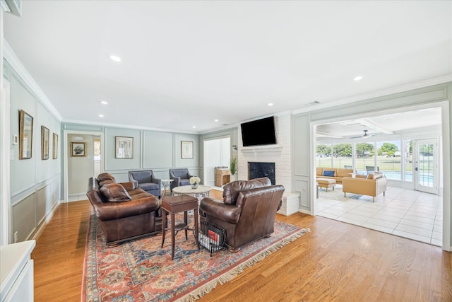 living room with a decorative wall, crown molding, a brick fireplace, and light wood-style floors