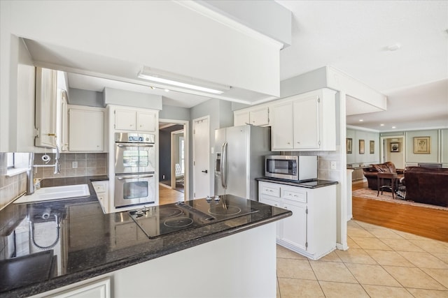 kitchen with a sink, open floor plan, white cabinetry, stainless steel appliances, and decorative backsplash