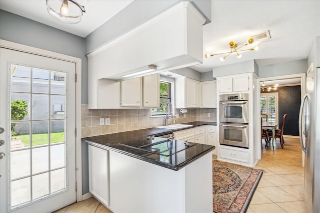 kitchen featuring a peninsula, a chandelier, dark countertops, a sink, and stainless steel appliances