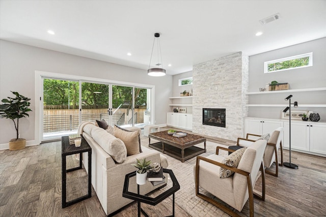 living room with visible vents, wood finished floors, a stone fireplace, and recessed lighting