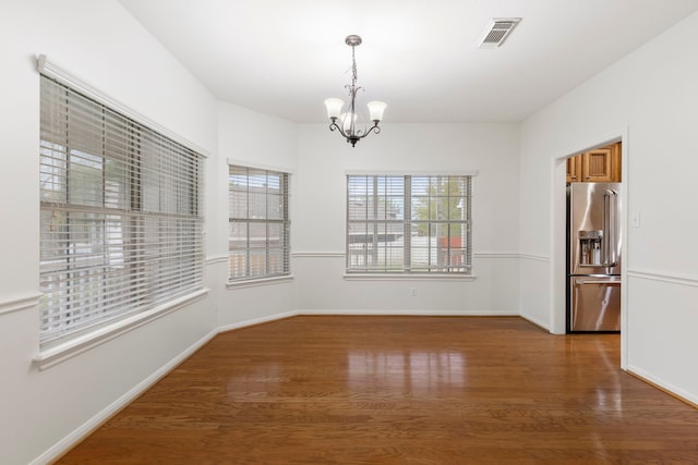 unfurnished dining area featuring visible vents, baseboards, a chandelier, and wood finished floors