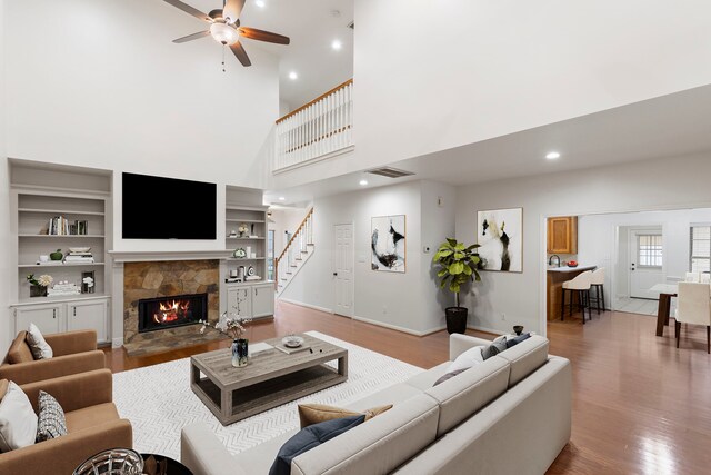 living room featuring a towering ceiling, light wood-type flooring, a fireplace, visible vents, and ceiling fan