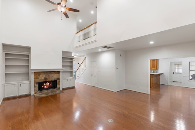 unfurnished living room featuring visible vents, a high ceiling, a stone fireplace, ceiling fan, and wood finished floors