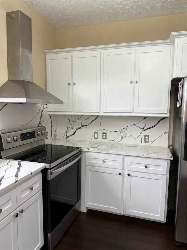kitchen featuring dark wood-type flooring, appliances with stainless steel finishes, wall chimney range hood, and white cabinetry