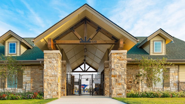 view of exterior entry with stone siding, roof with shingles, and a gate