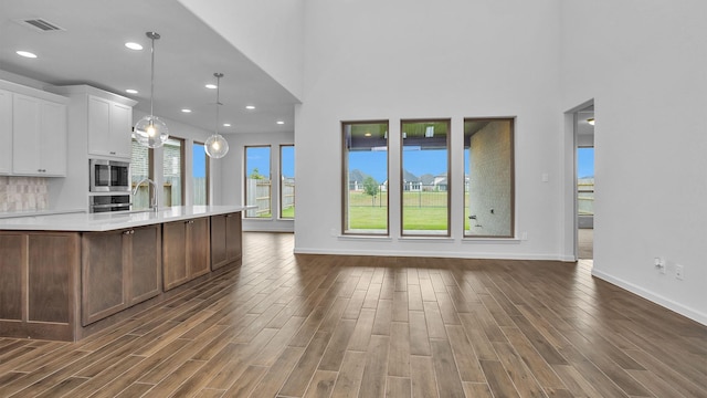 kitchen featuring stainless steel appliances, light countertops, dark wood-type flooring, baseboards, and a towering ceiling