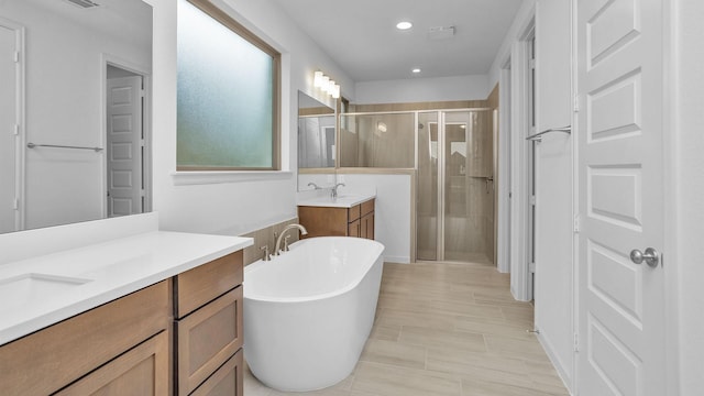 bathroom featuring a shower stall, two vanities, recessed lighting, and a freestanding bath