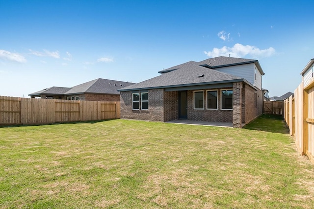 rear view of property featuring a fenced backyard, brick siding, a shingled roof, a yard, and a patio