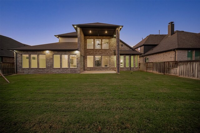rear view of house with brick siding, a fenced backyard, a lawn, and a patio area
