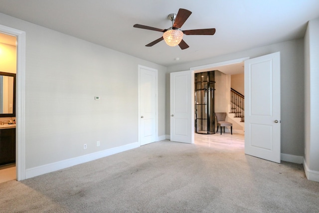 unfurnished bedroom featuring light carpet, ensuite bath, baseboards, and a ceiling fan