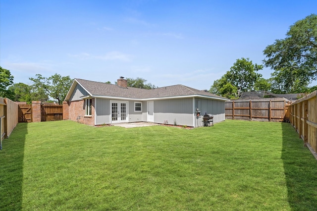 rear view of property with french doors, a fenced backyard, a yard, and a chimney
