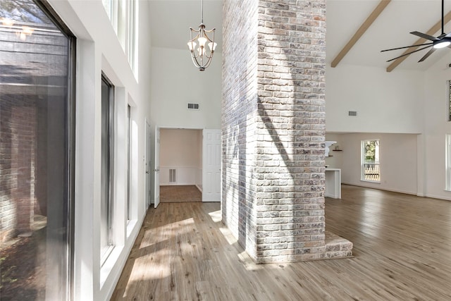foyer entrance with high vaulted ceiling, wood finished floors, visible vents, and ceiling fan with notable chandelier