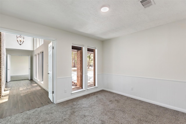 unfurnished room featuring a textured ceiling, wainscoting, a chandelier, carpet floors, and visible vents