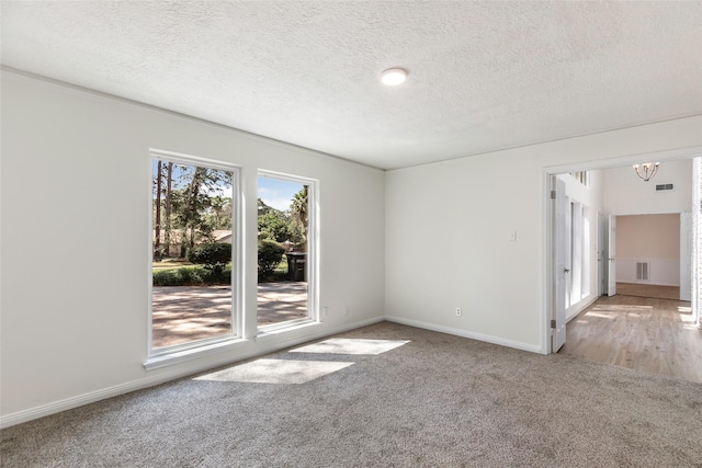 carpeted empty room featuring an inviting chandelier, a textured ceiling, visible vents, and baseboards