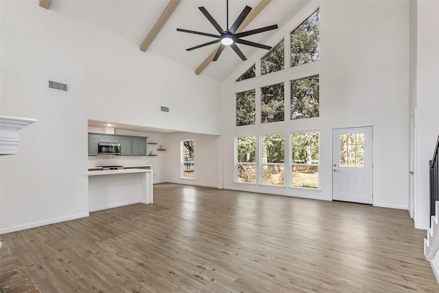 unfurnished living room featuring light wood-style flooring, baseboards, beamed ceiling, ceiling fan, and high vaulted ceiling