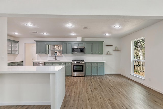kitchen featuring open shelves, stainless steel appliances, light countertops, and green cabinetry