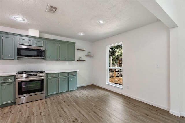 kitchen with a textured ceiling, light wood-style floors, green cabinets, stainless steel appliances, and visible vents