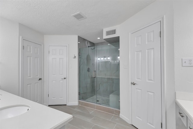 full bathroom featuring a shower stall, vanity, a textured ceiling, and visible vents