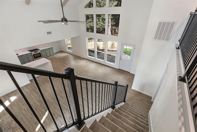 staircase featuring high vaulted ceiling, baseboards, wood finished floors, and visible vents