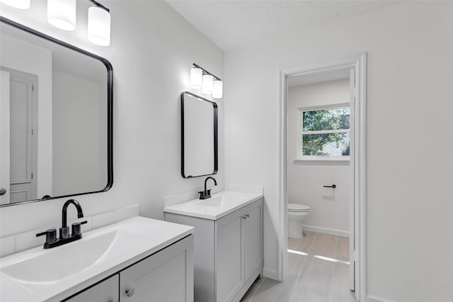 full bath featuring two vanities, baseboards, a sink, and toilet