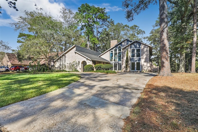 view of front of home with a chimney, a front yard, and concrete driveway