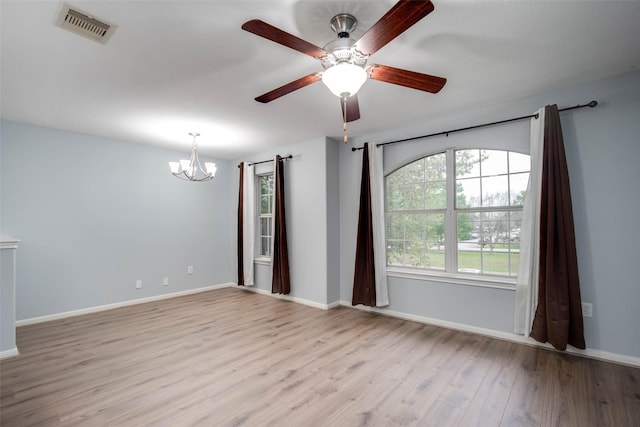 empty room with wood finished floors, ceiling fan with notable chandelier, baseboards, and visible vents