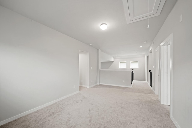 empty room featuring baseboards, attic access, and light colored carpet