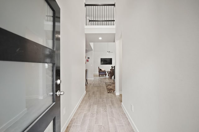 hallway with light wood finished floors, a towering ceiling, and baseboards