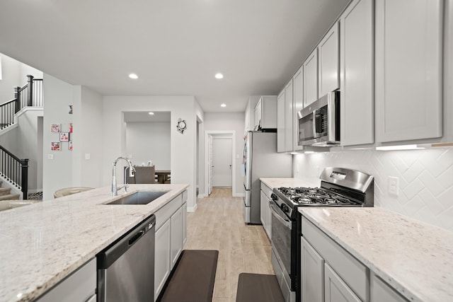 kitchen with appliances with stainless steel finishes, light wood-type flooring, light stone counters, decorative backsplash, and a sink