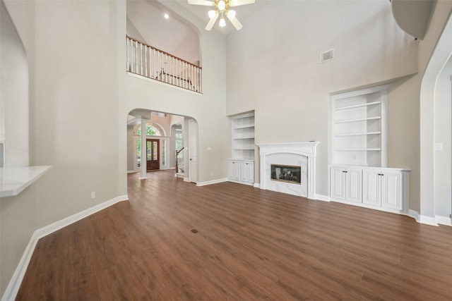 unfurnished living room with arched walkways, a ceiling fan, wood finished floors, and baseboards