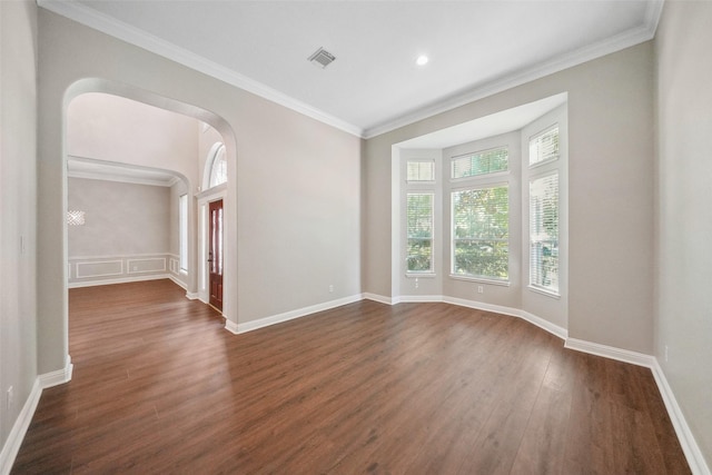 spare room featuring visible vents, ornamental molding, dark wood-type flooring, arched walkways, and baseboards